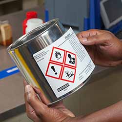 An employee attaches a GHS label to a chemical container.