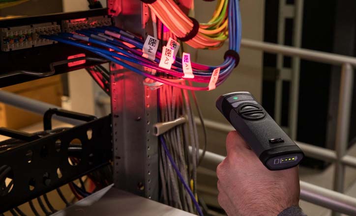 An employee scans Brady electrical barcode labels attached to networking cables, demonstrating the ISO barcode standard.