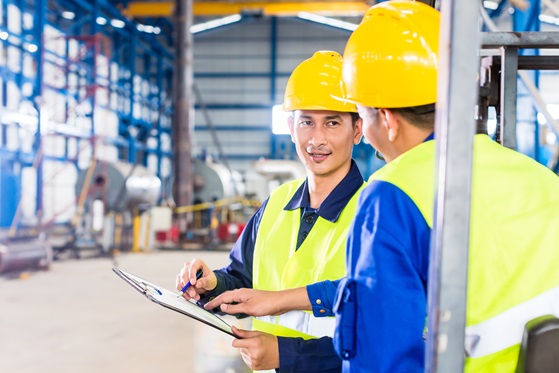 An inspector points to a checklist of safety hazards for a forklift driver.