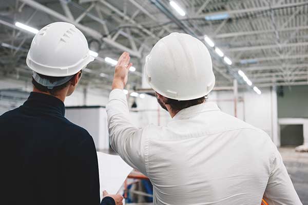 Two workers wearing hard hats. One is pointing out a safety hazard to the other.