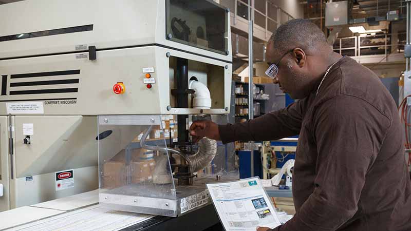 A worker inspecting a laser cutter in a warehouse environment to ensure equipment longevity.