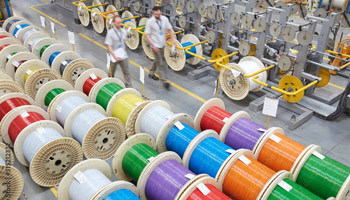 Alt text: Large wheels of colorful fiber optic cables are lined up on a warehouse floor.