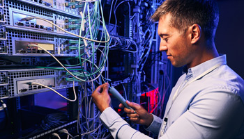 A data center employee inspects fiber optic cables with green and grey outer jackets.