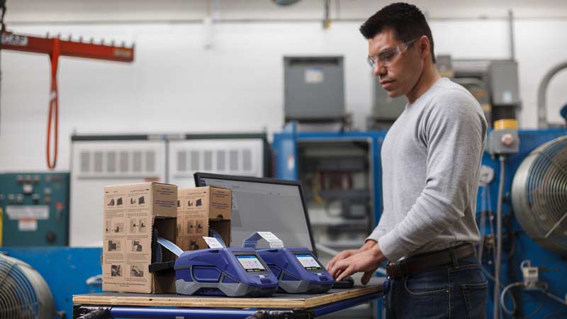 A man in a warehouse setting is creating heat shrink labels on Brady M611 label printer.