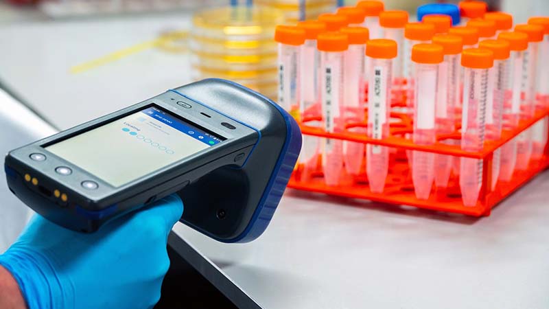 Scientist scanning multiple test tubes placed on a storage rack using an RFID scanner in a laboratory environment, meticulously recording the data.