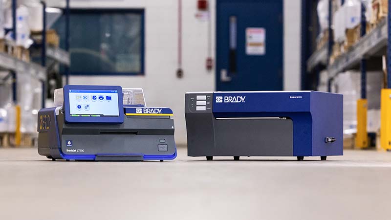 Brady J7300 and J4000 Inkjet benchtop printers sitting on a table in a warehouse setting.