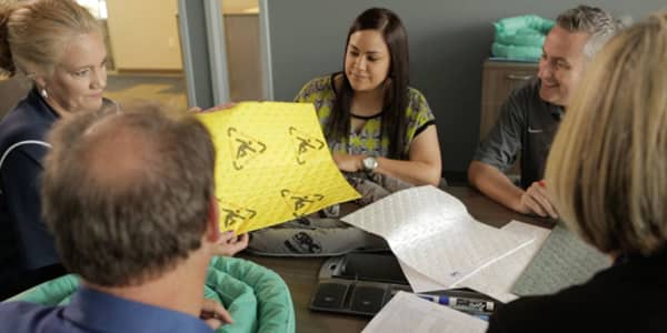 A safety leader trains a group of employees on HazCom safety practices while holding an absorbent pad.