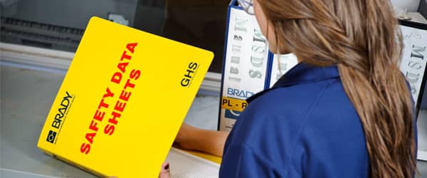 A warehouse worker reads through a binder containing GHS Safety Data Sheets.