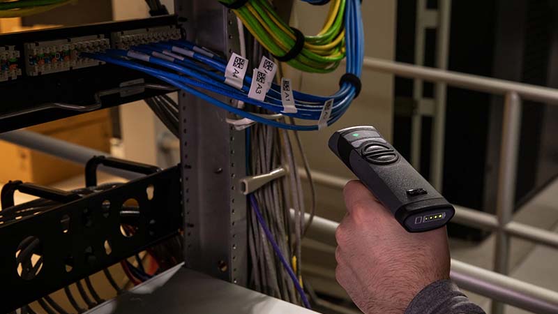 A worker scans QR codes on network rack labels in an industrial setting.